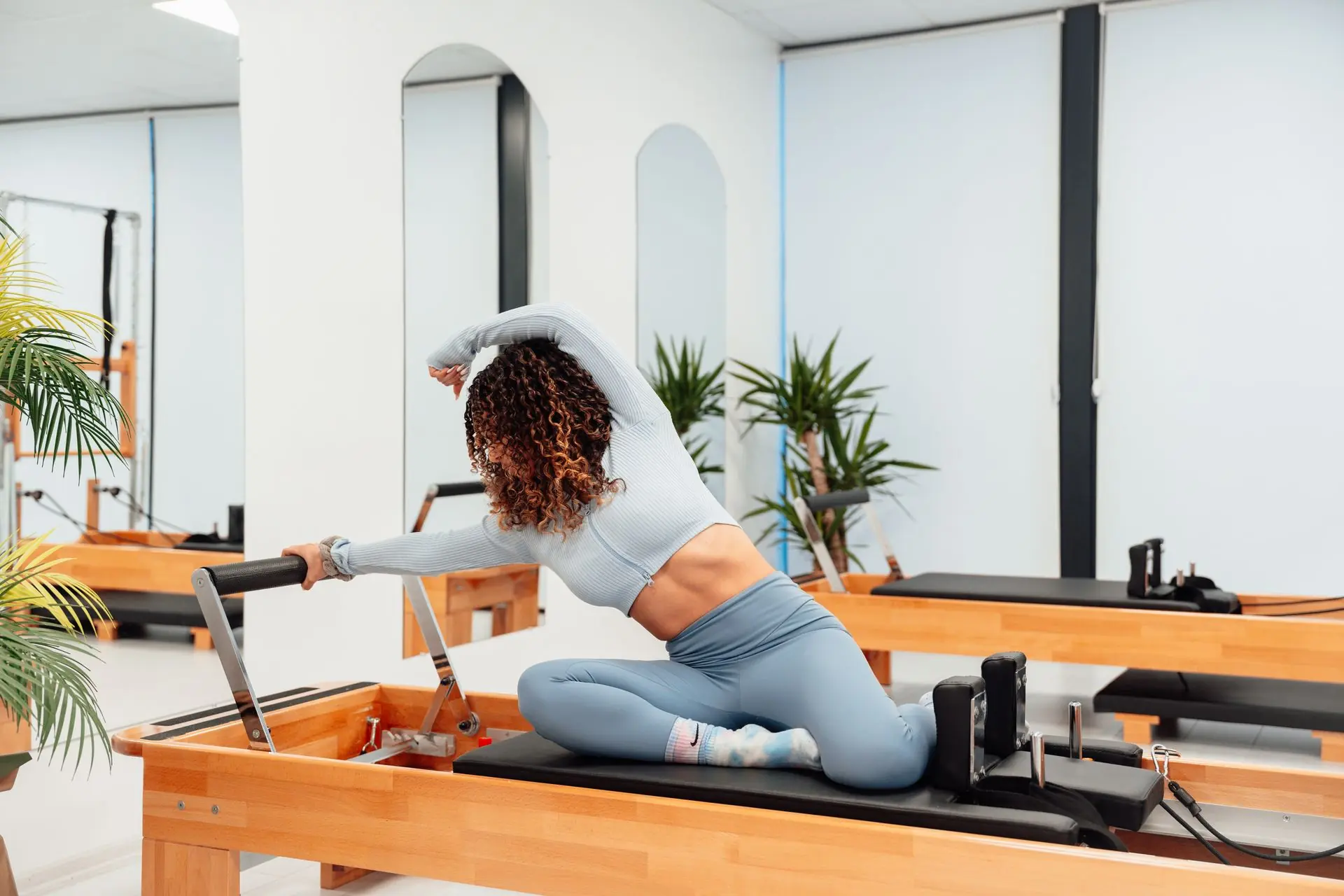 Praticante de Pilates em alongamento lateral sobre o Reformer, em um estúdio iluminado