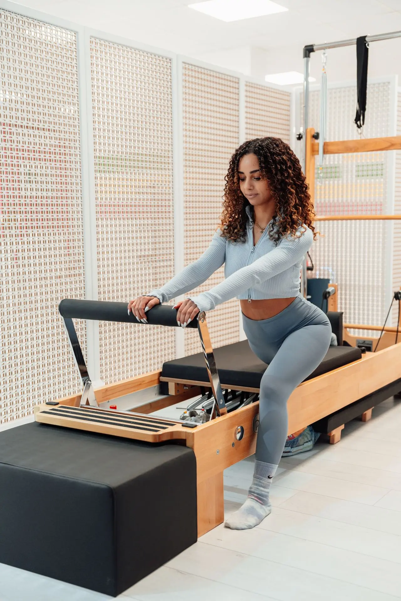 Praticante de Pilates em um Reformer, com os braços apoiados na barra e o olhar atento ao movimento